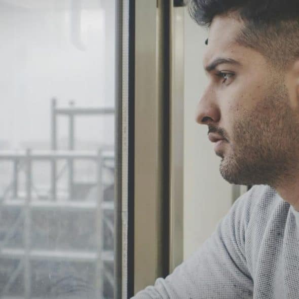 A man gazes out a window with an industrial scene visible outside.