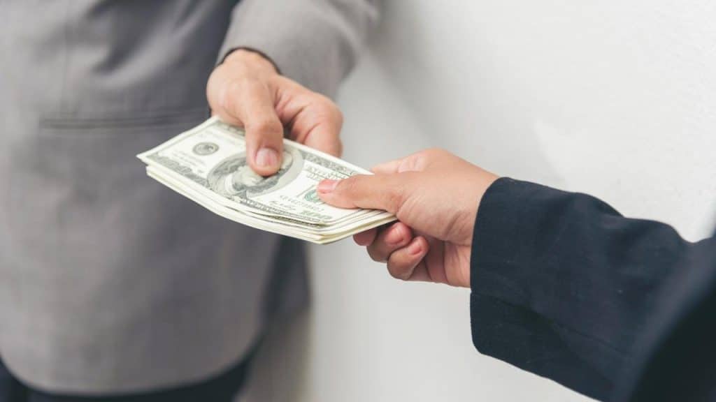 A stack of U.S. dollar bills being passed between two hands