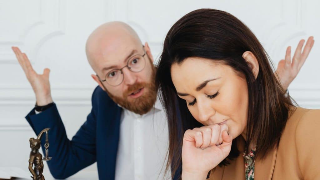 A man with glasses making fun of his partner who looks perturbed with closed eyes.