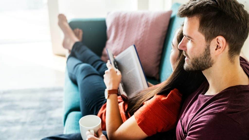 A women reading a book laying on the shoulder of her husband