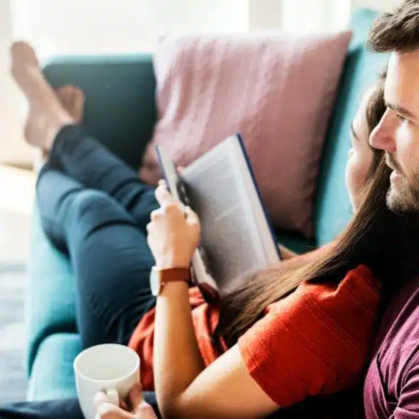 A women reading a book laying on the shoulder of her husband
