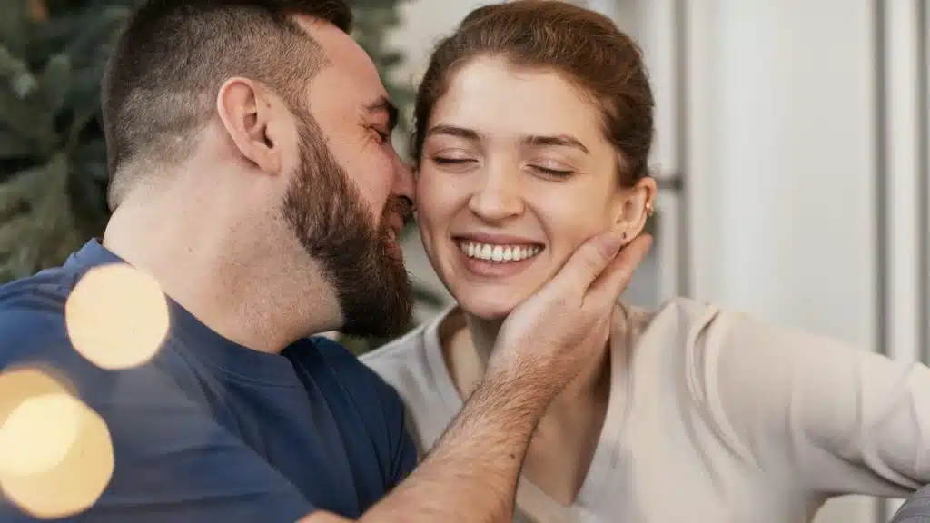 A bearded man about to kiss a smiling woman’s cheek.