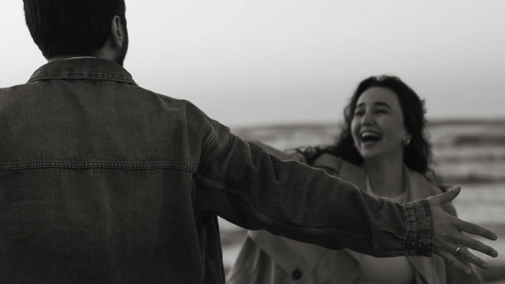 A man with open hands standing in front of a laughing woman who is coming towards him