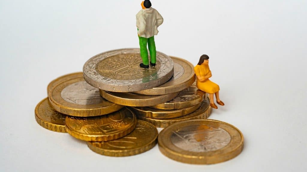 A man toy is standing on the stacks of coins while women is sitting while a women toy sitting beneath it