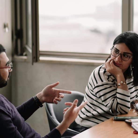 A man and woman discussing work at a table with a laptop.