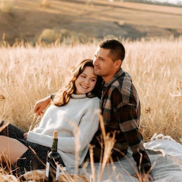 A woman laying in the lap of her husband while they are sitting in a field.