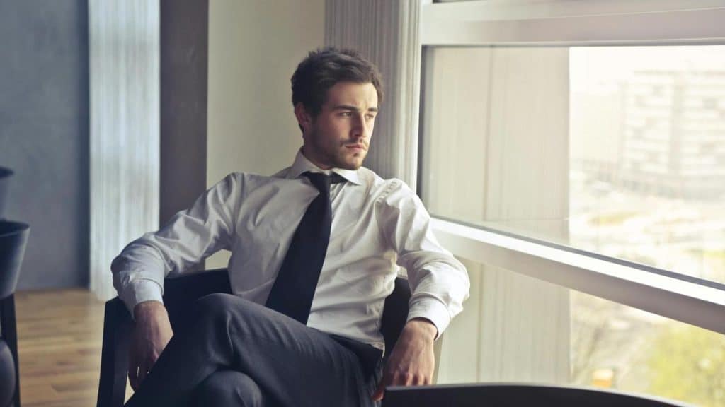A man in a white shirt and tie sitting by a window