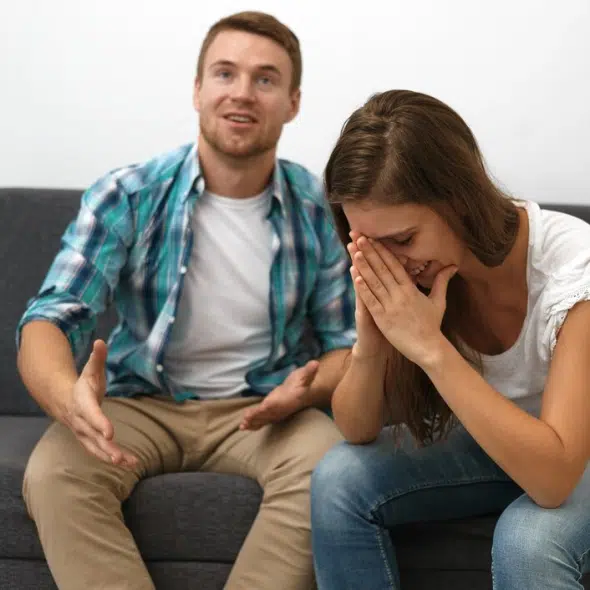 Man happy on couch, with woman holding her head in hands beside