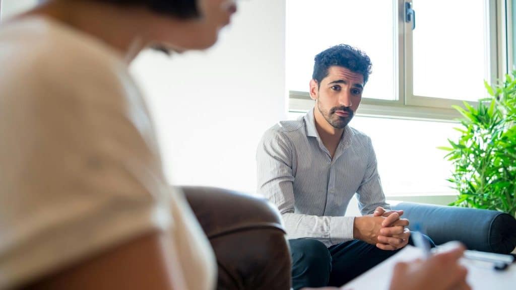 A man sitting on a couch talking to someone taking notes.