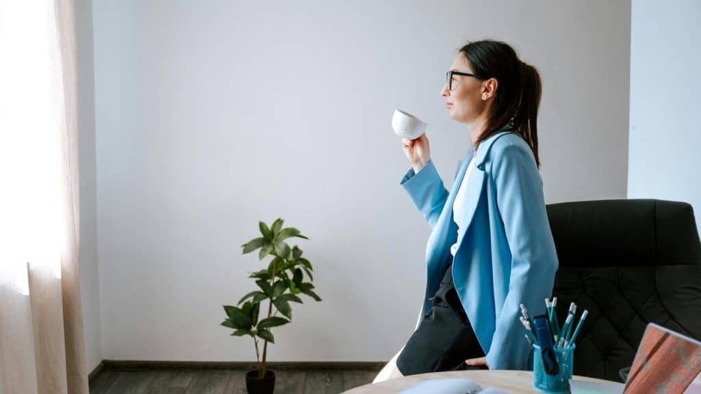 A woman in an office holding a cup and looking out a window.
