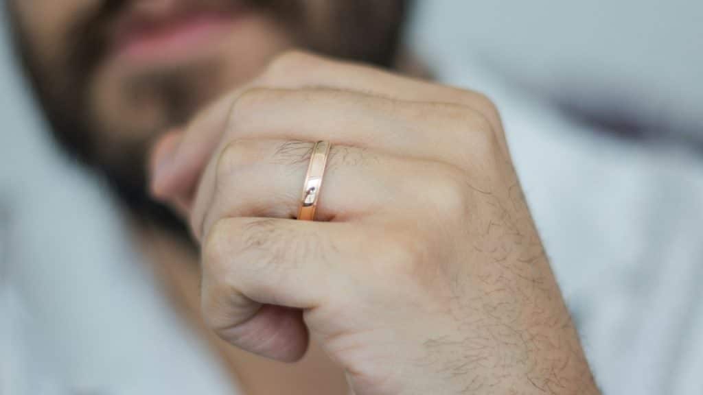 A close-up view of a person's hand wearing a plain gold band on their ring finger.