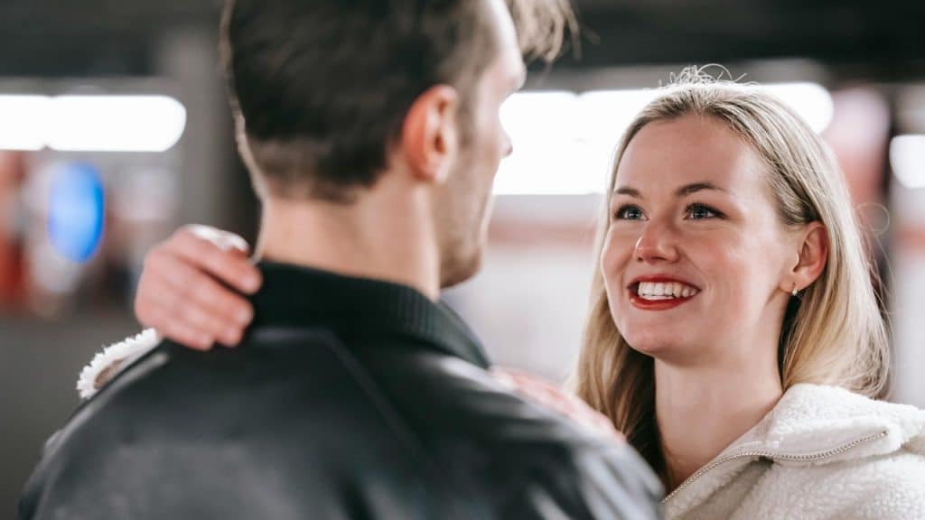 A smiling woman looks at a man while resting her hand on his upper back.