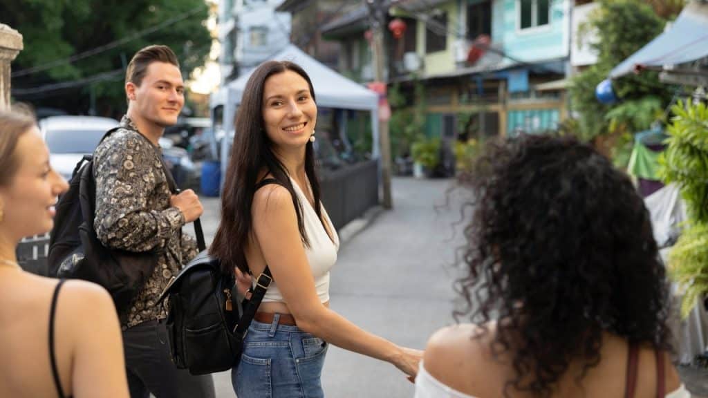 A woman with a black backpack smiles while walking down a street with three people.