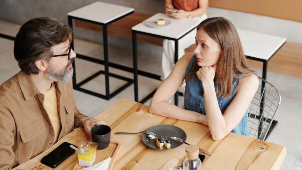 A woman in a denim top rests her chin on her hand at a table.