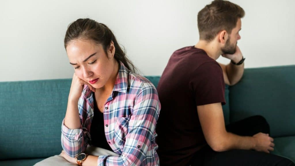 A man and woman sit back-to-back on a blue sofa looking in opposite directions.