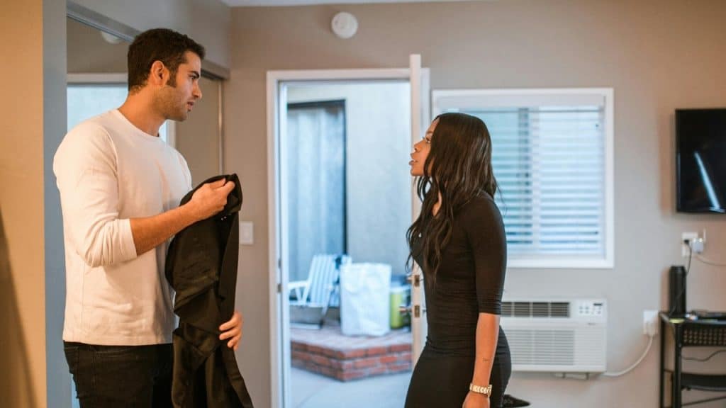 A man in a white shirt and a woman in black stand talking in a room.