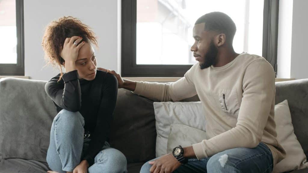 A man places a hand on the shoulder of a woman who is touching her forehead.