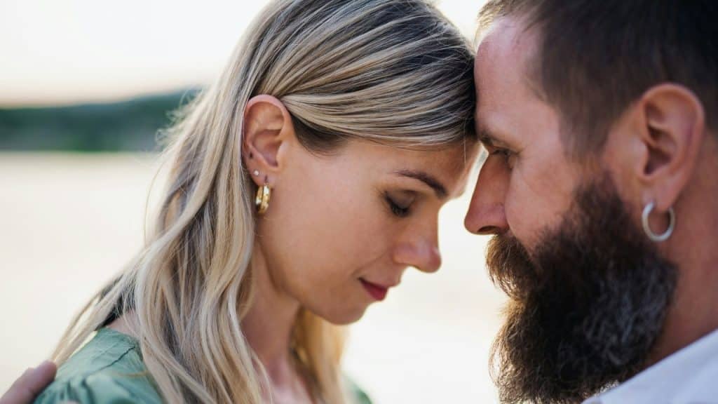 A close-up profile shot of a man and a woman pressing their foreheads together gently.