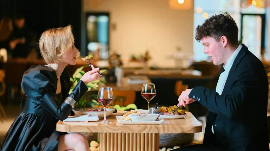 A woman and a man sit at a wooden table eating dinner in a restaurant.