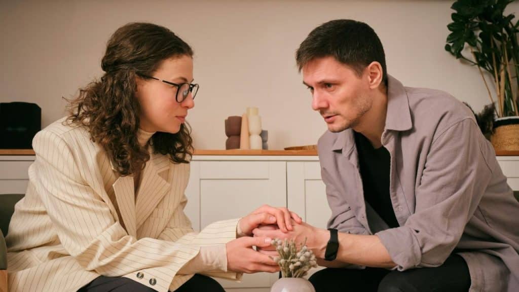 A man and woman sit together while holding hands over a small wooden table.