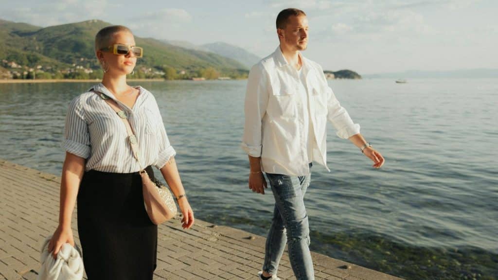A man and woman walk along a paved path next to a body of water.