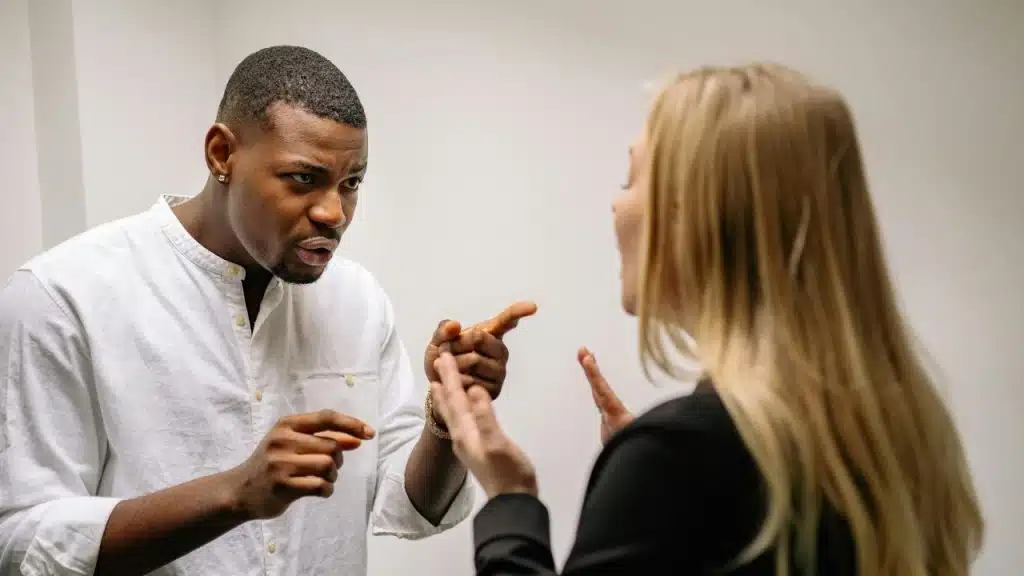 A man in a white shirt points his finger while talking to a blonde-haired woman.