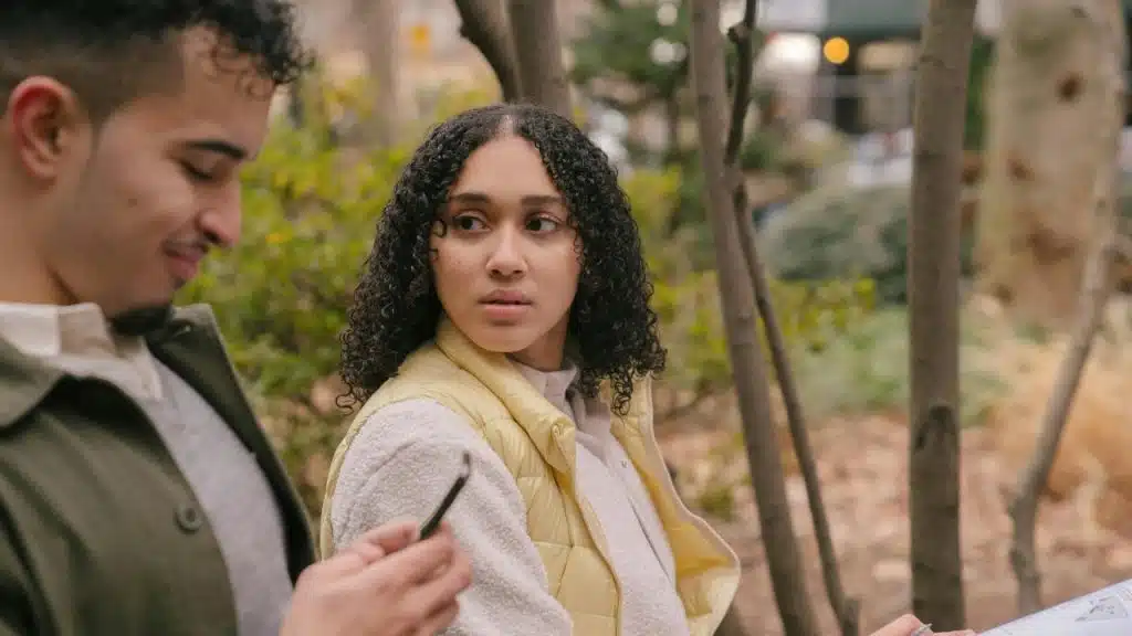 A woman looks toward a man who is smiling and looking down at his phone.