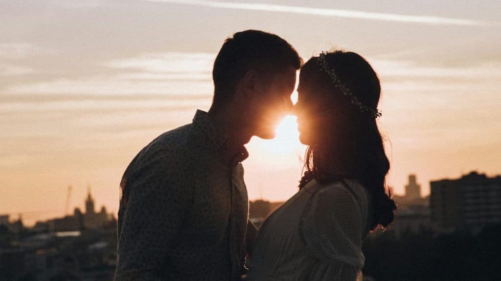 Silhouette of a couple kissing at sunset with a city skyline in the background.