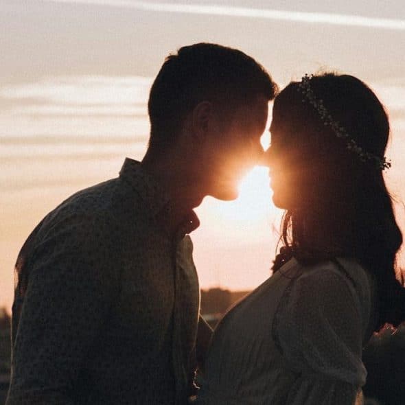 Silhouette of a couple kissing at sunset with a city skyline in the background.