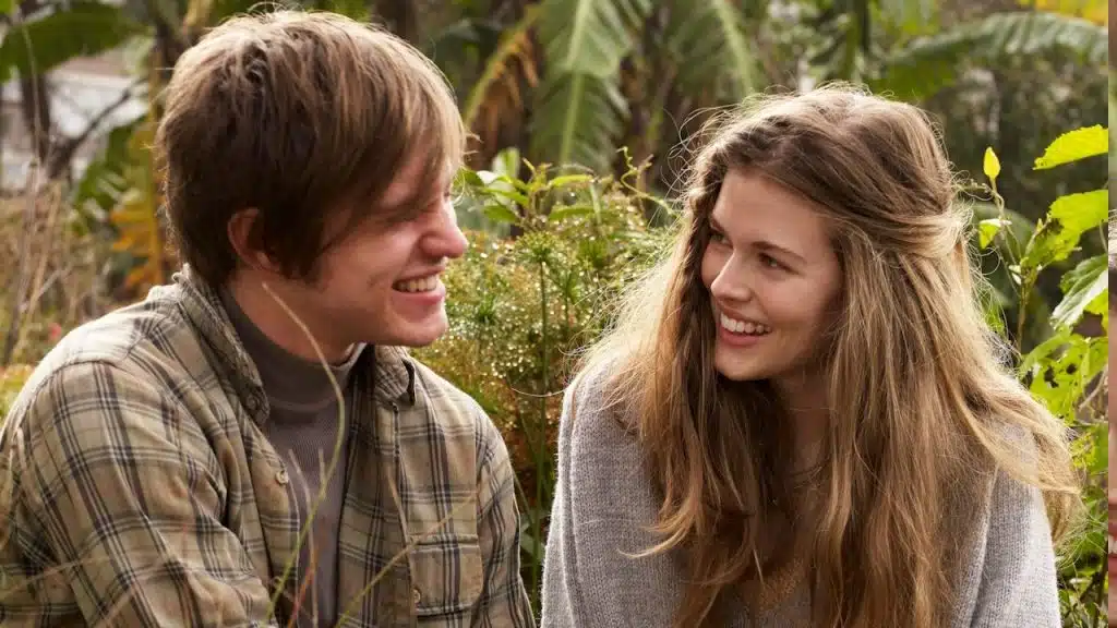 A couple smiling at each other while sitting in front of some plants.