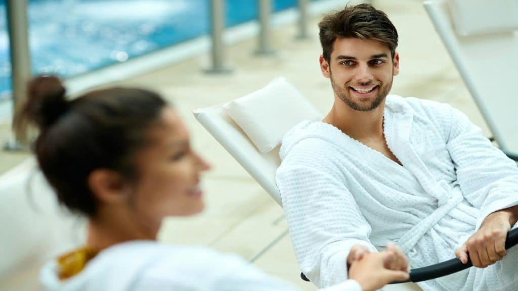 A young happy couple in bathrobes holding hands.
