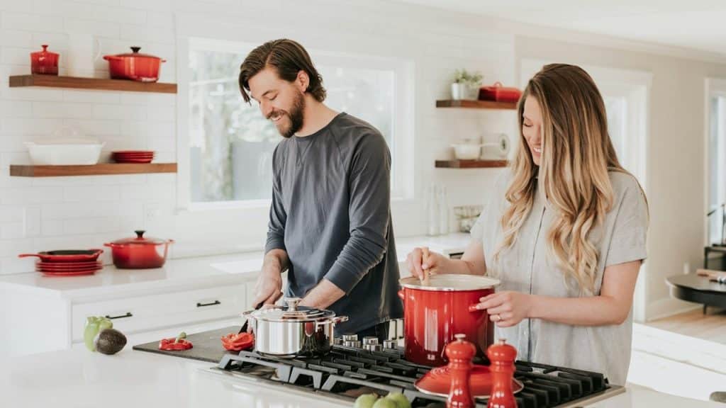 A man and a woman cooking in their tidy kitchen.