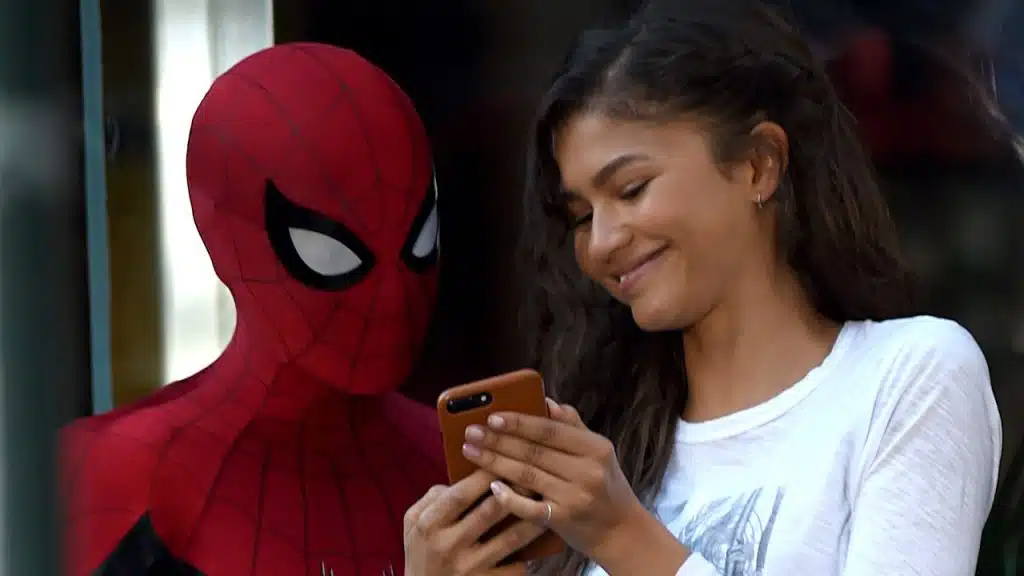 A picture of Zendaya showing something to Tom Holland, who is dressed as Spider-Man.