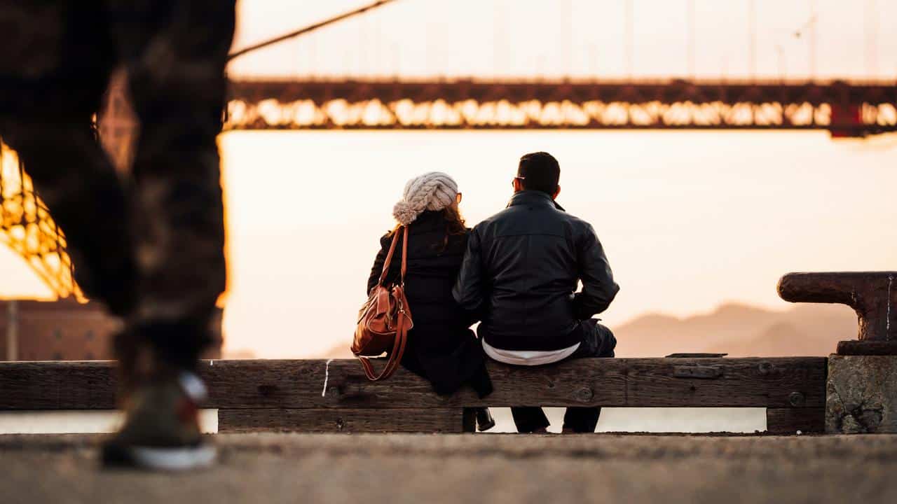 A couple sitting on a bench by the water at sunset.