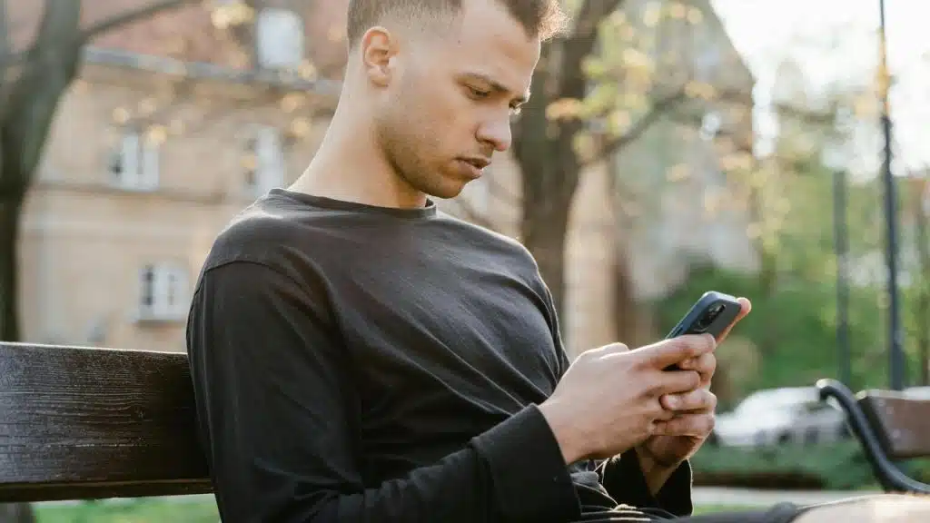A man sits on a park bench, focused on his phone.