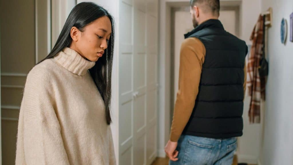 A woman looking down while a man stands turned away in a hallway.