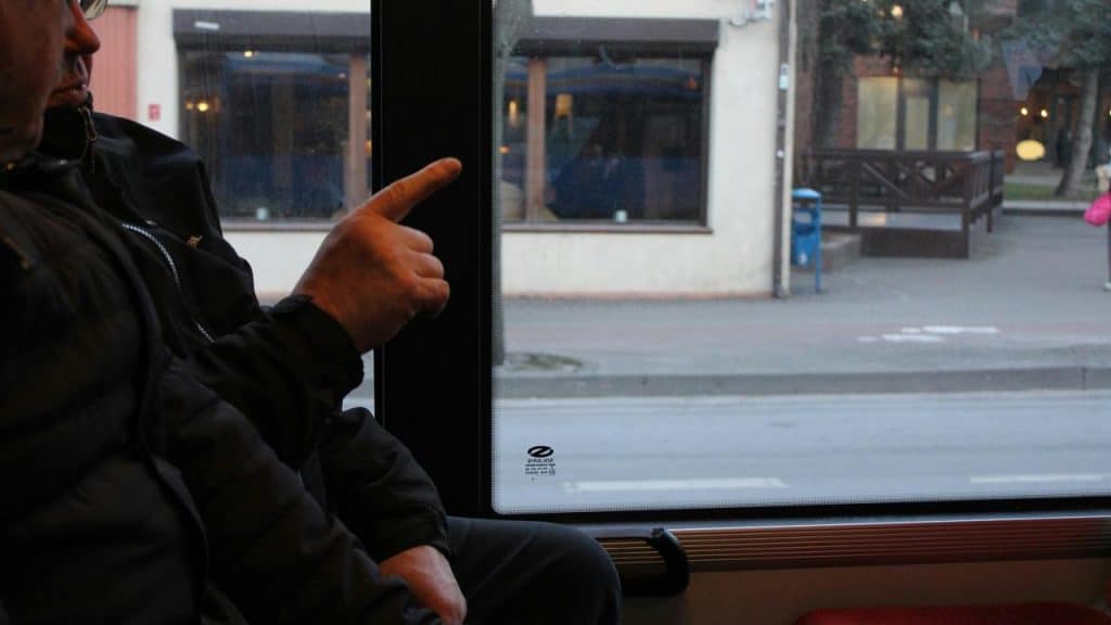 A person sitting by a window pointing outside from a bus or train.