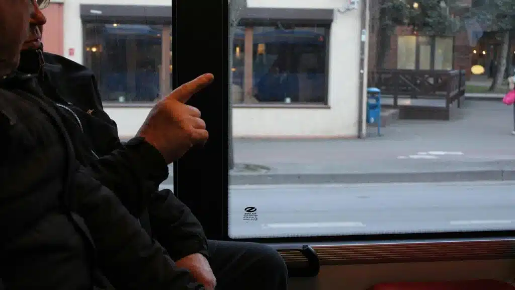 A person sitting by a window pointing outside from a bus or train.