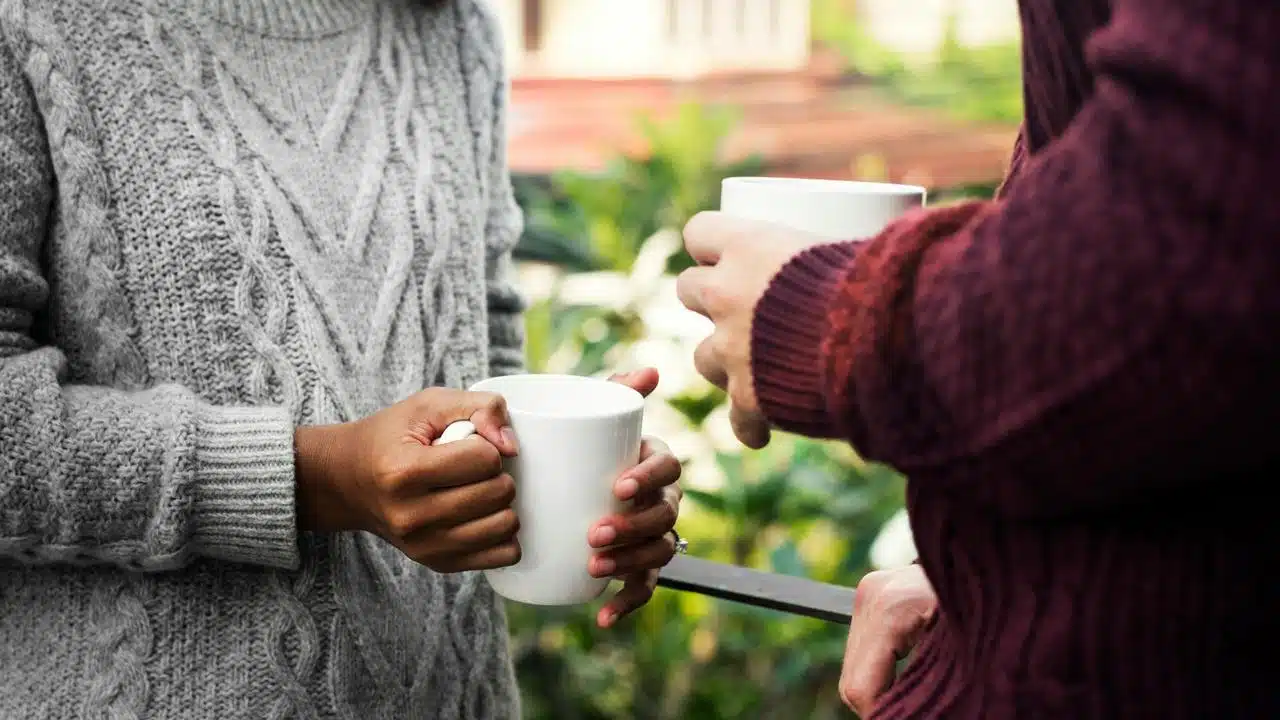 A couple holding coffee mugs while talking outdoors.