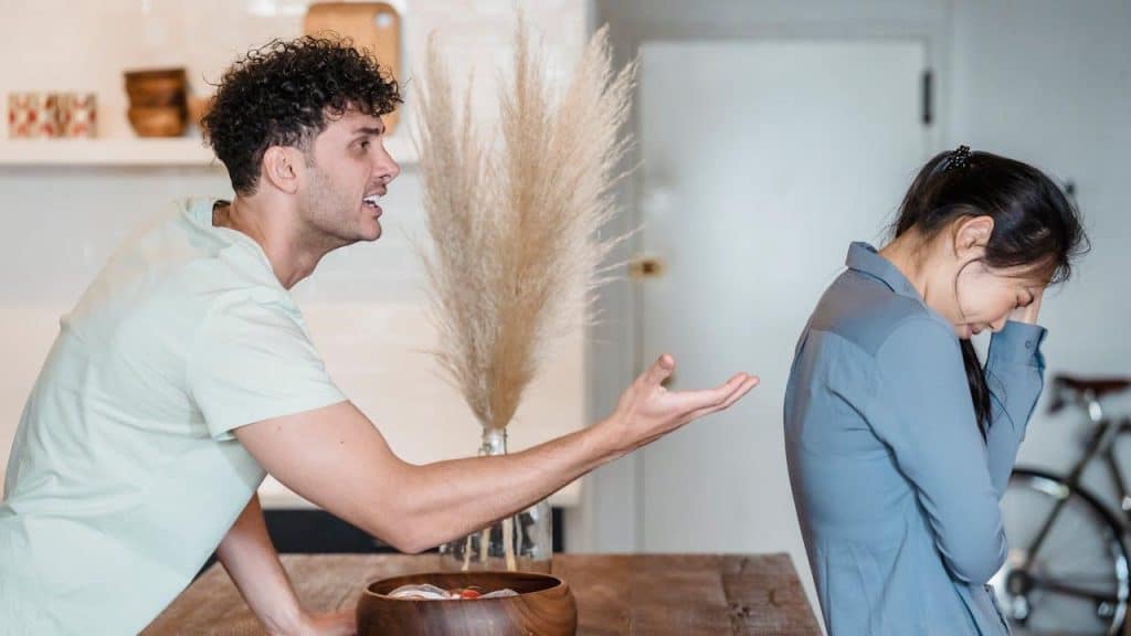 A man is aggressively yelling and gesturing at a woman who is turned away from him.