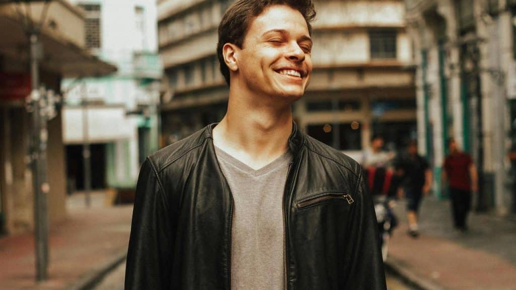 A smiling man in a black leather jacket standing on a city street.