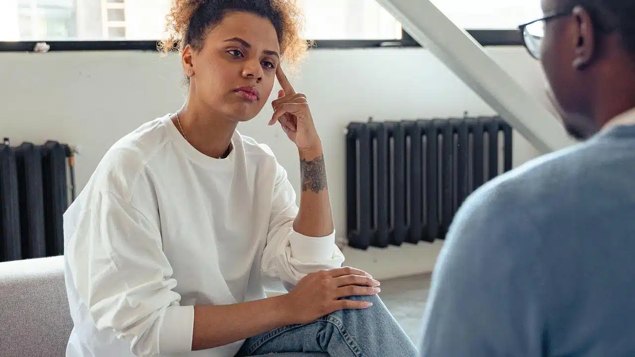 A woman listening thoughtfully to another person during a conversation indoors.
