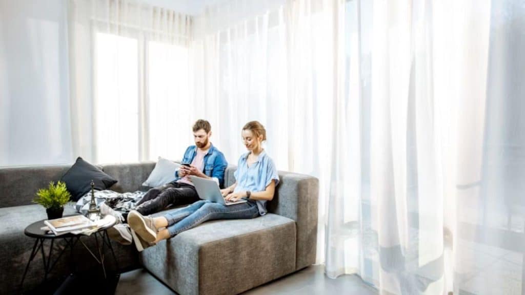 A couple sitting on a couch, both focusing on screens during a conversation