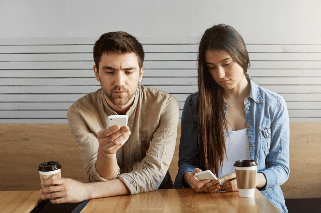 Young couple sitting at table checking phones