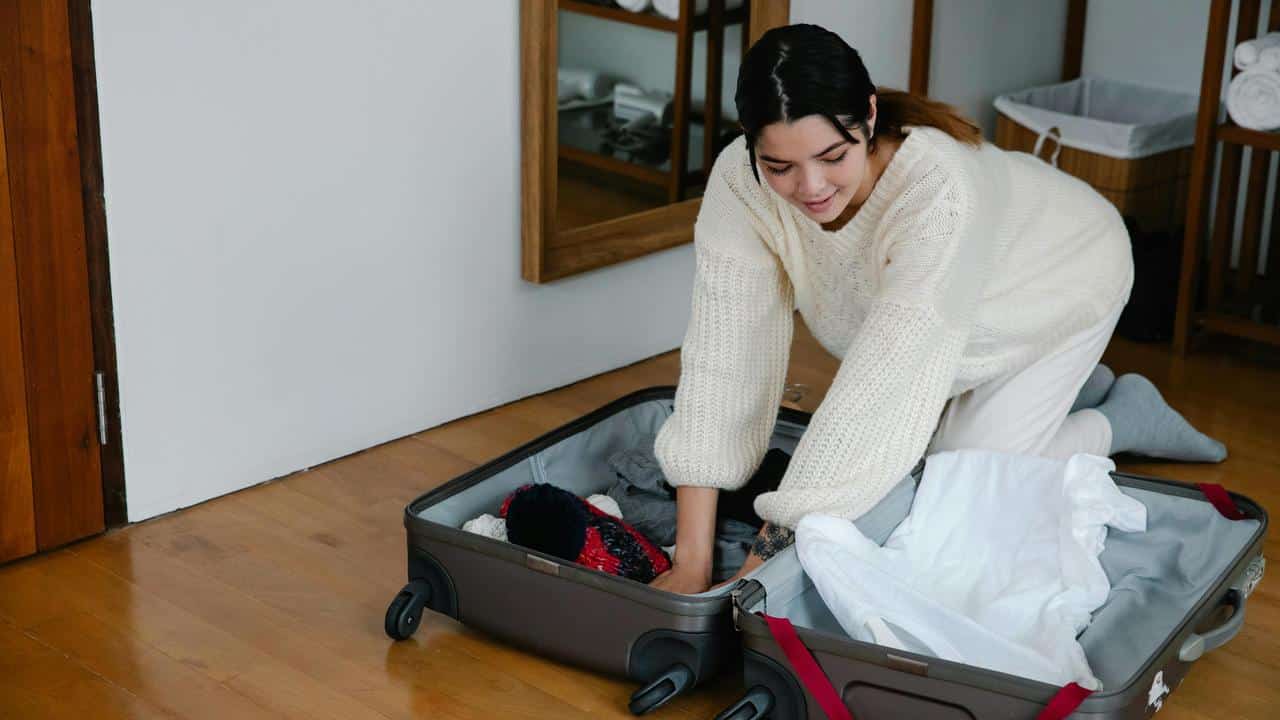 A woman packing clothes into a suitcase on the floor.