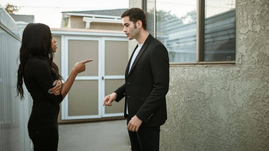 A man and woman arguing outside, with the woman pointing at him.