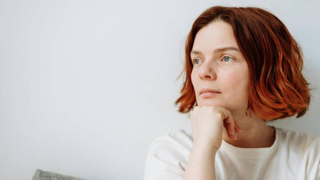 A woman with short red hair resting her chin on her hand and looking off thoughtfully.