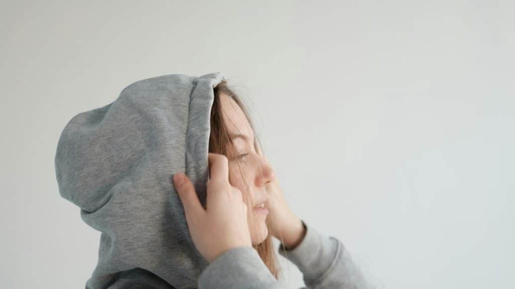 A woman pulling up her hoodie with her eyes closed, appearing calm or introspective.