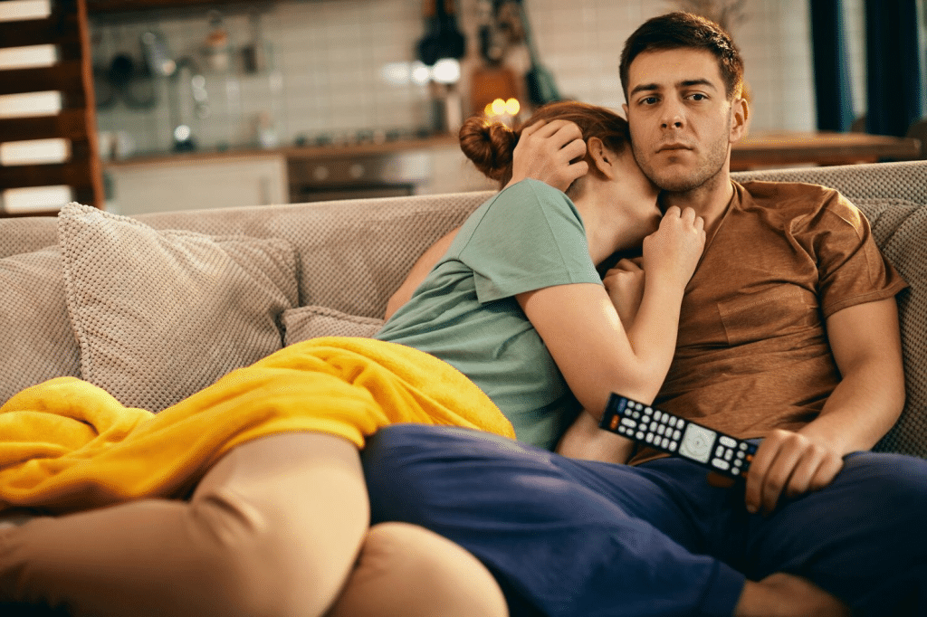 A man looking bored with woman cuddling him
