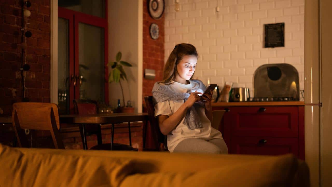 A woman sitting in a cozy kitchen at night, using her phone.
